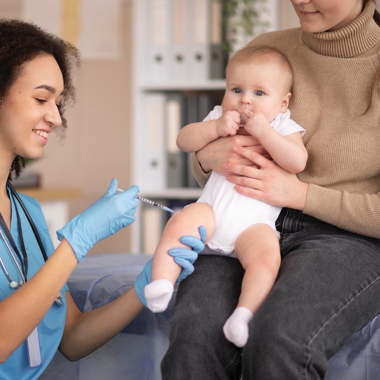 Een zorgverlener met blauwe handschoenen dient een vaccin toe aan een baby die op schoot zit bij een volwassene. De baby kijkt omhoog en de zorgverlener lacht vriendelijk.