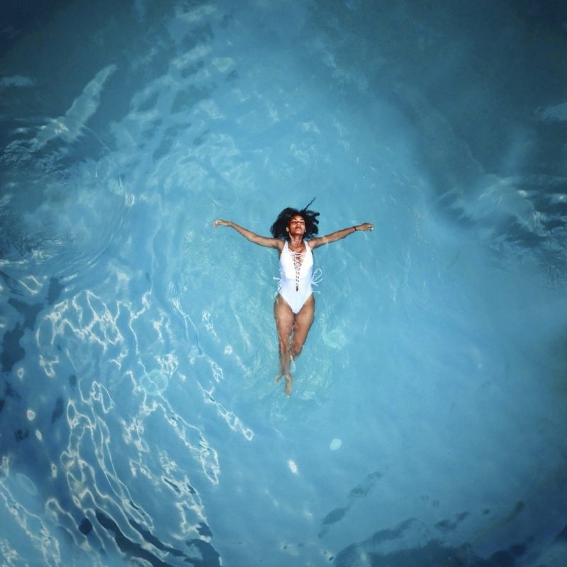 Een gelukkige zwangere vrouw zwemt ontspannen in een helder blauw zwembad, genietend van het veilige zwemmen tijdens zwangerschap in de zomerzon.
