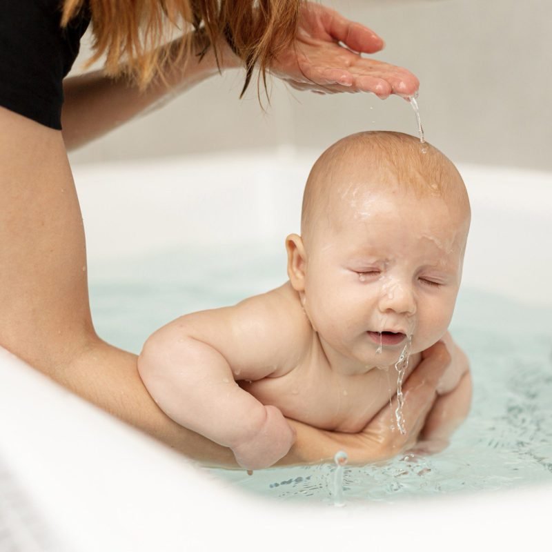 Moeder helpt haar baby in bad doen in een klein babybadje